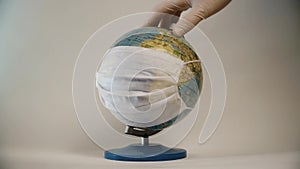 Hand in gloves rotate Earth globe with medical mask isolated on white background, global pandemic covid-19, coronavirus