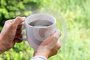 Hand golding big white cup of hot black coffee with nature morning view