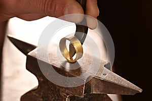 Hand of a goldsmith punches a hallmark into a golden ring on an