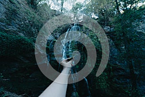 Hand grabbing a fern in front of a dark waterfall in the middle of the forest