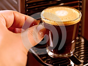 Hand grabbing glass of coffee espresso machine closeup