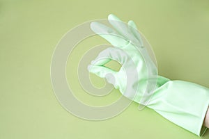 Hand in green rubber glove showing Ok symbol on green background for design with copy space. Concept for cleaning, medicine,