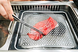 Hand grilling a medium rare slice of Kagoshima Wagyu A5 beef with marble texture with tongs, grilled on metal yakiniku pan.