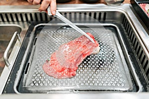 Hand grilling a medium rare slice of Kagoshima Wagyu A5 beef with marble texture with tongs, grilled on metal yakiniku pan.