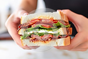 hand griping blt sandwich before a bite