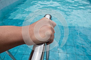 Hand gripping the rail of the swimming pool stainless steel ladder