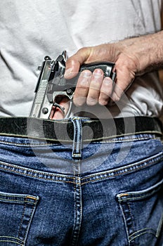 Hand gripping silver 9mm handgun in waistband view from behind