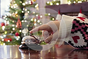 Hand of guest ringing reception bell on desk of guesthouse, hotel at christmas time. Color shining garland on christmas tree