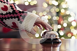 Hand of guest ringing reception bell on desk of guesthouse, hotel at christmas time. Color shining garland on christmas tree