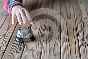 Hand of guest ringing in silver bell. on wooden rustic reception desk with copy space. Hotel service. Selective focus.