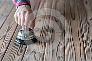 Hand of guest ringing silver vintage bell on wooden rustic reception desk with copy space. Hotel, restaurant.
