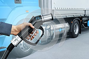 Hand with H2 fueling nozzle on a background of hydrogen fuel cell semi truck with