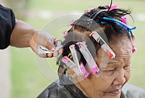 Hand of a hairstylist doing a perm rolling hair of senior woman