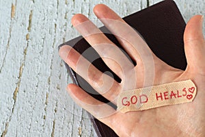 Hand with handwritten quote God heals on a bandage on top of holy bible book