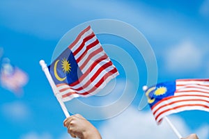 Hand happily waving Malaysia flag against blue sky