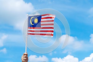 Hand happily waving Malaysia flag against blue sky photo