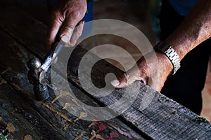 Hand of a hardworking person holding a hammer and working on a wooden table