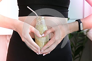 Hand in heart symbol holding smoothie drink detox on fit and slim belly woman. Fitness wellbeing concept. Body care