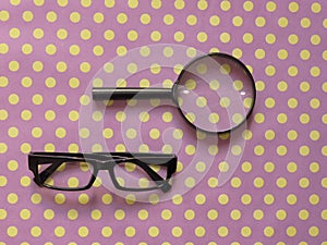 Hand-Held Reading Magnifier, Magnifying Glass, a Pair of Glasses with black frame on spotted dotty patterned background.