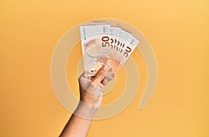 Hand of hispanic man holding 50 euro banknotes over isolated yellow background