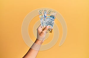 Hand of hispanic man holding australian 50 dollars banknotes over isolated yellow background