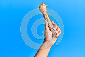 Hand of hispanic man holding dog bone over isolated blue background