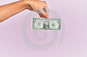 Hand of hispanic man holding one dollar banknote over isolated pink background
