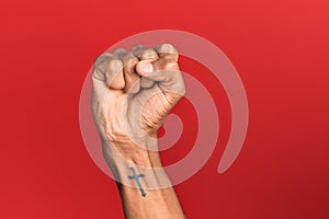 Hand of hispanic man over red isolated background doing protest and revolution gesture, fist expressing force and power