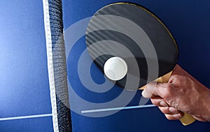 Hand hitting a ball with table tennis paddle on table