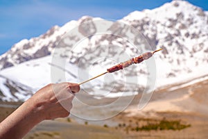 hand hold Arrosticino - typical Abruzzese sheep skewer - grilled with mountains of Gran Sasso background in Campo