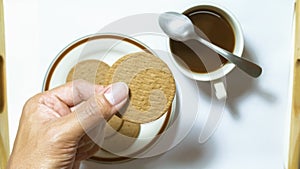 Hand hold brown biscuits in dish pairing with black coffee with