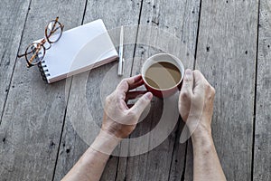 Hand hold cup of coffee and empty notebook on wooden table