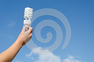 Hand hold energy saving lamp blue sky background
