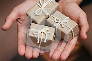Hand hold the gift box. Present wrapped in craft paper and satin ribbon. Small parcel in a girls hands. Christmas time.