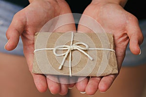 Hand hold the gift box. Present wrapped in craft paper and satin ribbon. Small parcel in a girls hands. Christmas time.