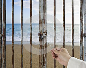 Hand hold key unlocking locked door, beach, ocean, sky background