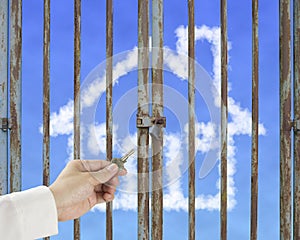 Hand hold key unlocking locked door with cloud house in blue sky