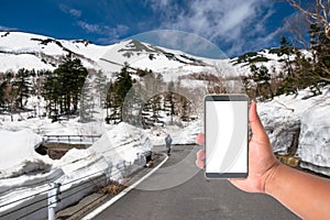 hand hold mobile phone with a road of snow wall japan alps mountain, Japan