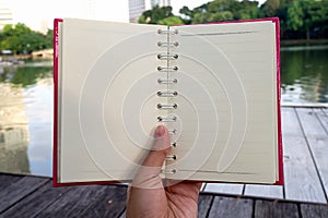 Hand hold opened white blank book with pink cover in the park and road in background