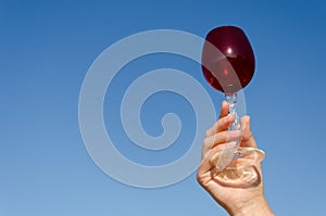 Hand hold red wineglass squirm stem on blue sky