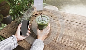 Hand hold smartphone or mobile phone and glass of green tea