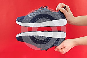 Hand hold sports shoes on red background. Holding new fashion sneakers for running. Choosing and buy of new sneakers