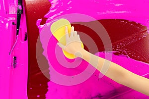 Hand hold yellow sponge over car for washing pink foam background. Top view