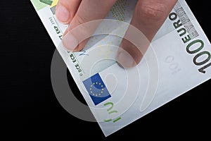 Hand holding 100 euro banknote on a black background