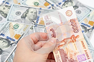 A hand holding 5000 rubles banknote over us dollar background, financial crisis and choosing currency for savings concept
