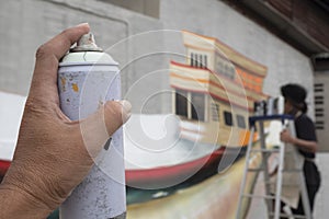 ` hand holding aerosol spray can with blurred street artist is painting graffiti on cement wall background