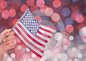 Hand holding American flag with sparkling light bokeh background