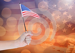 Hand holding American flag with sparkling light bokeh background