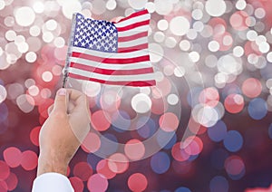 Hand holding American flag with sparkling light bokeh background