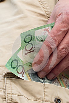 Hand holding australian dollars 100 banknotes in the pocket of cargo shorts. Tradie finance concept